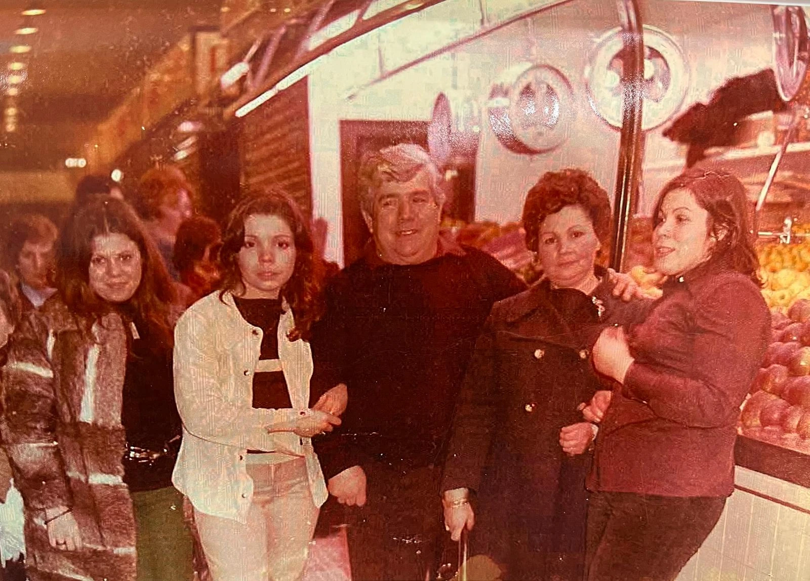 Un grup de persones al costat d’una parada de fruita, en una fotografia antiga del mercat