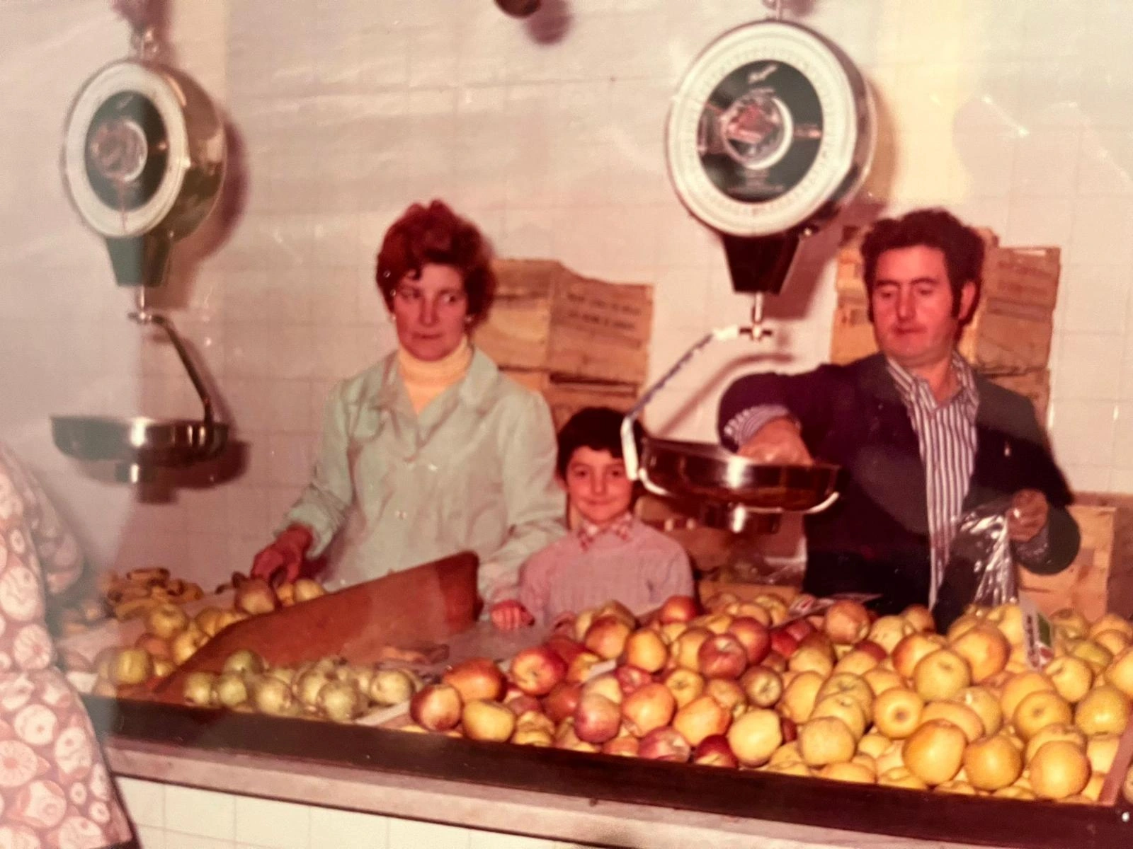 Fotografia històrica d’una família darrere d’un taulell de fruita, amb balances i caixes al fons