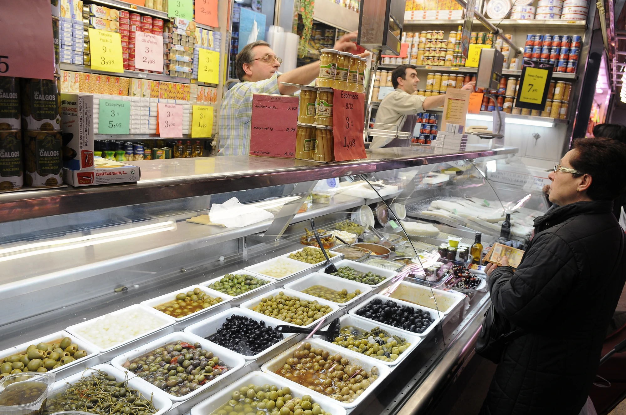 Una parada d’olives i conserves amb una clienta davant del taulell